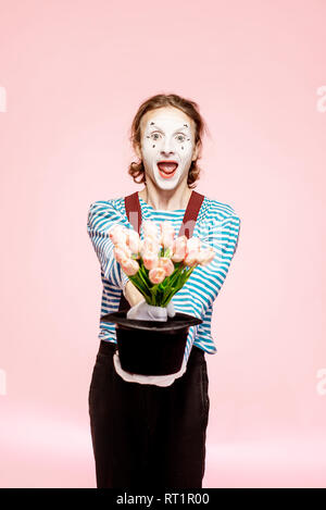 Emotional pantomime posing with tulip bouquet on the pink background indoors. Valentine's Day and love concept Stock Photo