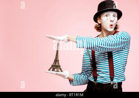 Pantomime with white facial makeup posing with Eiffel tower on the pink background. French mime concept Stock Photo