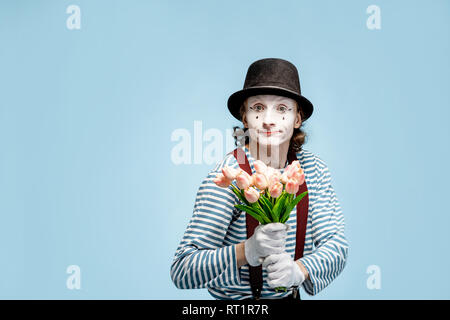 Emotional pantomime posing with tulip bouquet on the blue background indoors. Valentine's Day and love concept Stock Photo