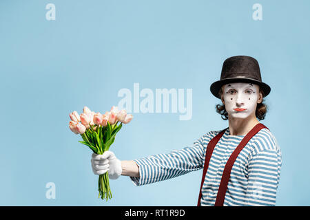 Emotional pantomime posing with tulip bouquet on the blue background indoors. Valentine's Day and love concept Stock Photo