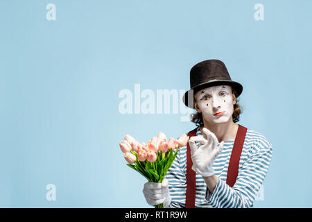 Emotional pantomime posing with tulip bouquet on the blue background indoors. Valentine's Day and love concept Stock Photo