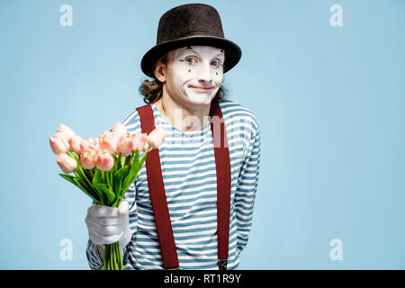 Emotional pantomime posing with tulip bouquet on the blue background indoors. Valentine's Day and love concept Stock Photo