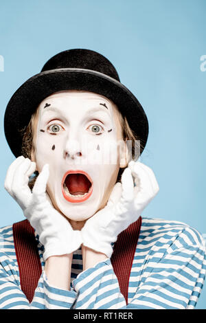 Close-up portrait of an actor as a pantomime with white facial makeup showing expressive emotions on the blue background Stock Photo