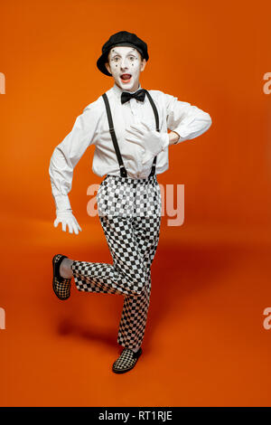 Full length portrait of an actor as a pantomime with white facial makeup showing expressive emotions on the orange background Stock Photo
