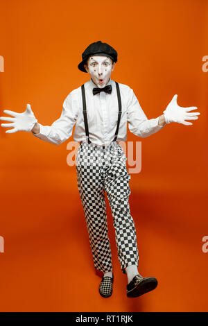 Full length portrait of an actor as a pantomime with white facial makeup showing expressive emotions on the orange background Stock Photo