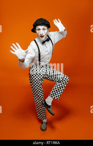 Full length portrait of an actor as a pantomime with white facial makeup showing expressive emotions on the orange background Stock Photo
