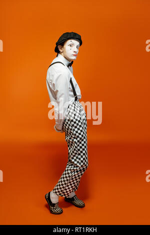 Full length portrait of an actor as a pantomime with white facial makeup showing expressive emotions on the orange background Stock Photo