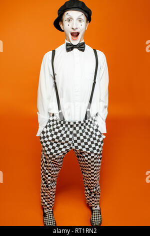 Full length portrait of an actor as a pantomime with white facial makeup showing expressive emotions on the orange background Stock Photo