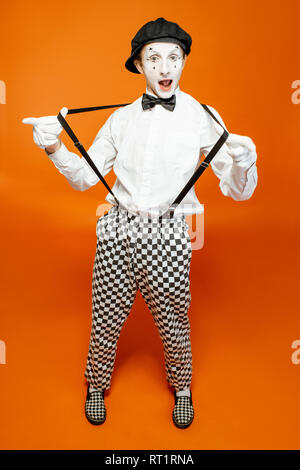Full length portrait of an actor as a pantomime with white facial makeup showing expressive emotions on the orange background Stock Photo