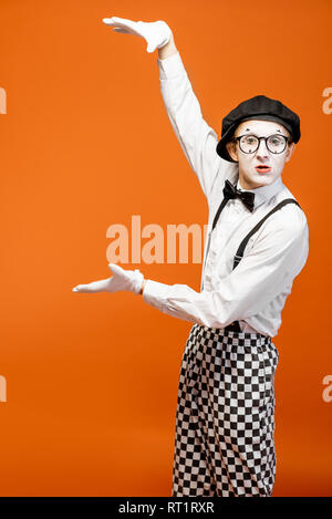 Emotional pantomime with white facial makeup showing empty space on the orange background, advertising something Stock Photo