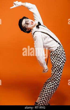 Emotional pantomime with white facial makeup showing empty space on the orange background, advertising something Stock Photo