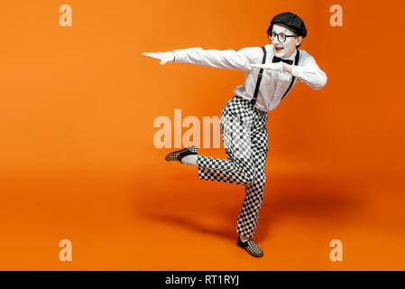 Emotional pantomime with white facial makeup showing empty space on the orange background, advertising something Stock Photo