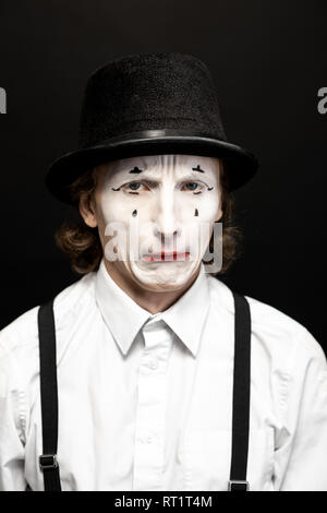 Close-up portrait of a pantomime with white facial makeup posing with expressive emotions on the black background Stock Photo