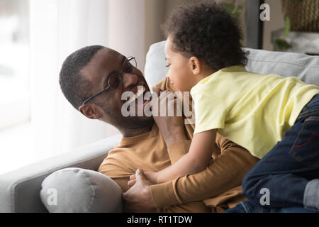 Happy african dad laughing playing with little toddler son together