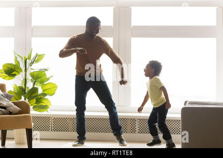 Happy african dad and toddler son dancing in living room Stock Photo