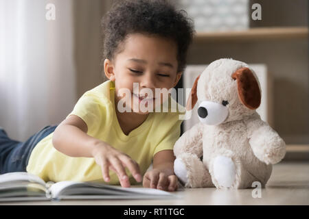 Happy african little boy playing alone reading book to toy Stock Photo