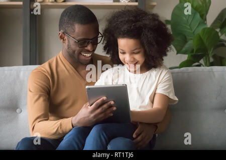 Happy african father and kid daughter using digital tablet Stock Photo