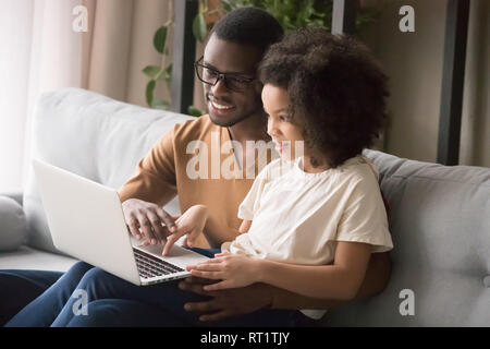 African dad and child daughter using laptop computer at home Stock Photo