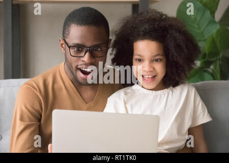 Surprised amazed black dad and kid daughter looking at laptop Stock Photo