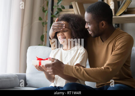 Loving african dad closing eyes of kid daughter making surprise Stock Photo