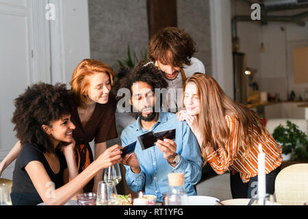 Friends sitting at dining table, looking at photographs Stock Photo