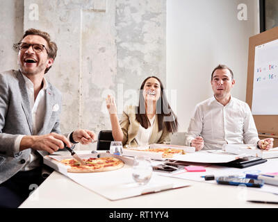 Laughing colleagues having lunch break with pizza in conference room Stock Photo