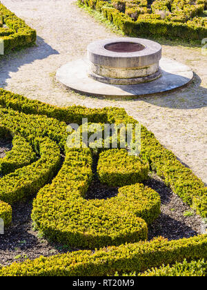 The parterre de broderie in the french formal garden of the castle of Auvers-sur-Oise with beds of boxwood pruned in geometrical shapes around a well. Stock Photo