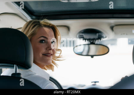 Smiling businesswoman in car turning round Stock Photo