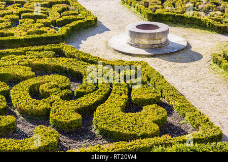 The parterre de broderie in the french formal garden of the castle of Auvers-sur-Oise with beds of boxwood pruned in geometrical shapes around a well. Stock Photo