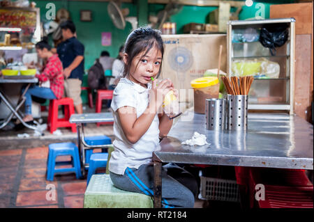 A little Cambodian girl relaxes with a much needed drink in a hot and busy indoor market in Phnom Penh Cambodia. Stock Photo