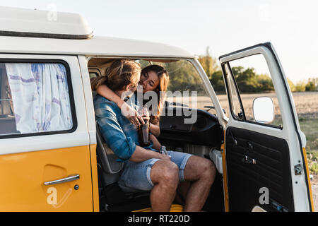 Happy couple sitting in their camper, embracing, drinking beverage Stock Photo