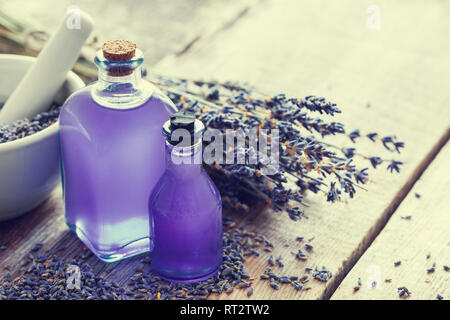 Two bottles of essential oil, mortar and lavender flowers bunch on table. Retro toned photo. Selective focus. Stock Photo