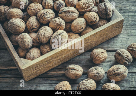 Walnuts in wooden box on old table, top view. Retro toned photo. Stock Photo