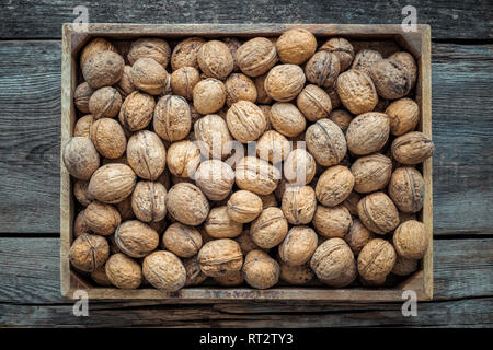 Walnuts in wooden box on old table, top view. Retro toned. Stock Photo