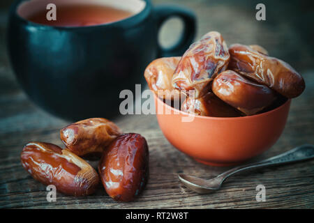 Dates fruits in bowl and tea cup on background. Retro toned photo. Stock Photo