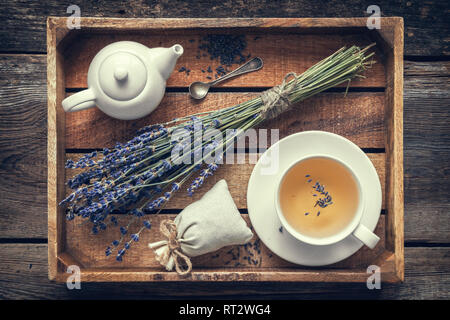 Bunch of lavender flowers, healthy tea in cup, teapot and sachets filled with dried lavender in wooden tray. Retro toned. Top view. Flat lay. Stock Photo