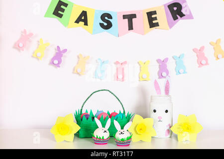 Diy decor for Easter. Paper garlands, vase bunny, daffodils, eggs bunnies, basket with painted eggs. Table decor, white room, home for Easter, spring. Stock Photo