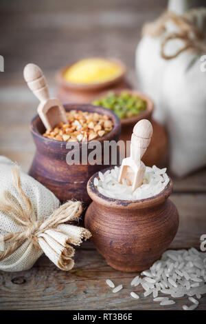 Rustic clay pots filled with rice, green mung, corn, buckwheat and sacks of grain on background. Stock Photo