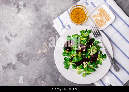Vegetarian salad of fresh raw vegetables lettuce beets on a white round plate on a gray background. Stock Photo