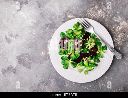 Vegetarian salad of fresh raw vegetables lettuce beets on a white round plate on a gray background. Stock Photo