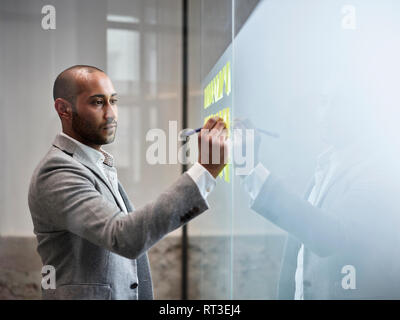 Businessman writing on sticky notes at glass pane in office Stock Photo