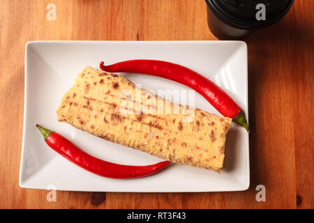 On a wooden background white square plate with Shawarma sandwich. Traditional Eastern snack. Fresh roll of thin lavash pita bread filled with grilled  Stock Photo