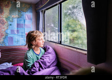 Boy in pyjama looking out of window of a camper Stock Photo