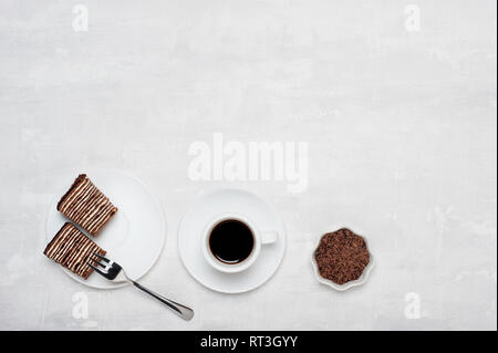Creative layout made of chocolate crumbs, cup with coffee and sweet chocolate cake on light grey background. Flat lay. Food concept. Stock Photo