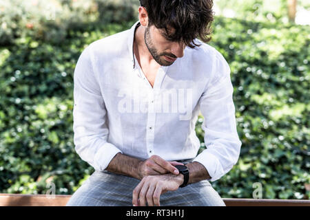 Young man sitting outdoors using smartwatch