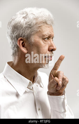 Serious senior frightened male keeps fore finger on lips, tries to keep conspiracy, says: Shh, make silence please. Isolated shot of man shows silence gesture Stock Photo