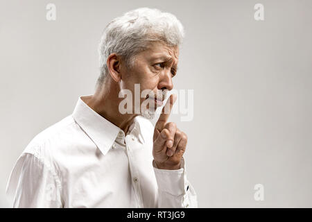 Serious senior frightened male keeps fore finger on lips, tries to keep conspiracy, says: Shh, make silence please. Isolated shot of man shows silence gesture Stock Photo