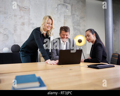 Businessman and two businesswomen sharing laptop in modern office Stock Photo