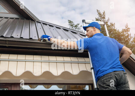 man standing on ladder and cleaning roof rain gutter from dirt Stock Photo