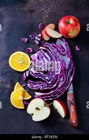 Sliced red cabbage, apples and orange slices on dark ground Stock Photo